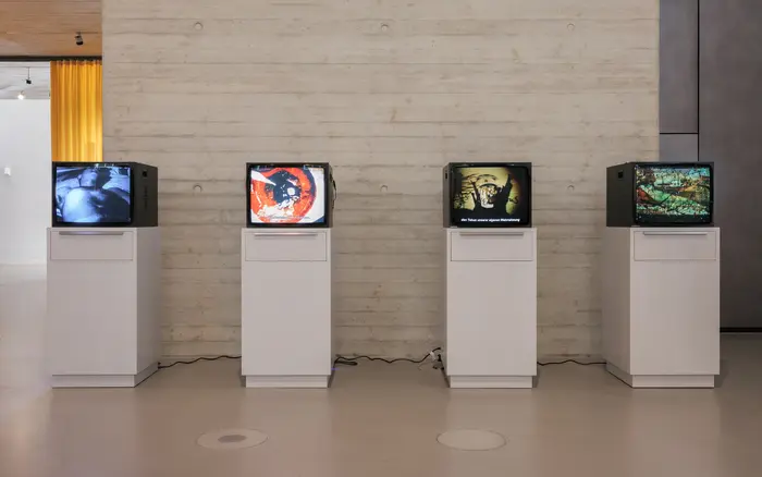 Vier nebeneinander aufgestellte Fernsehgeräte in einem Ausstellungsraum.