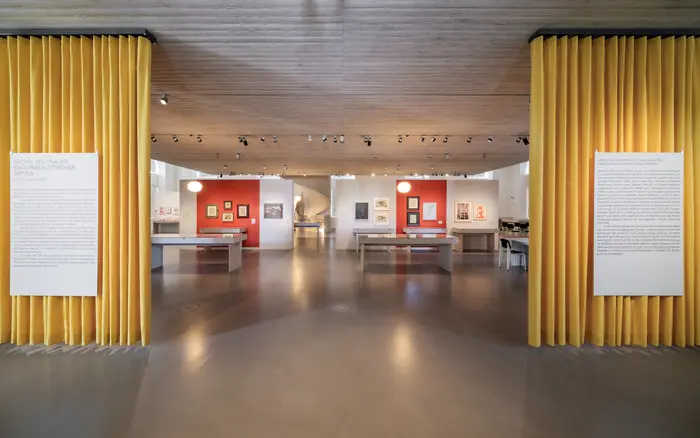 Ein Ausstellungsraum mit gelben Vorhängen und orangefarbenen Wänden.