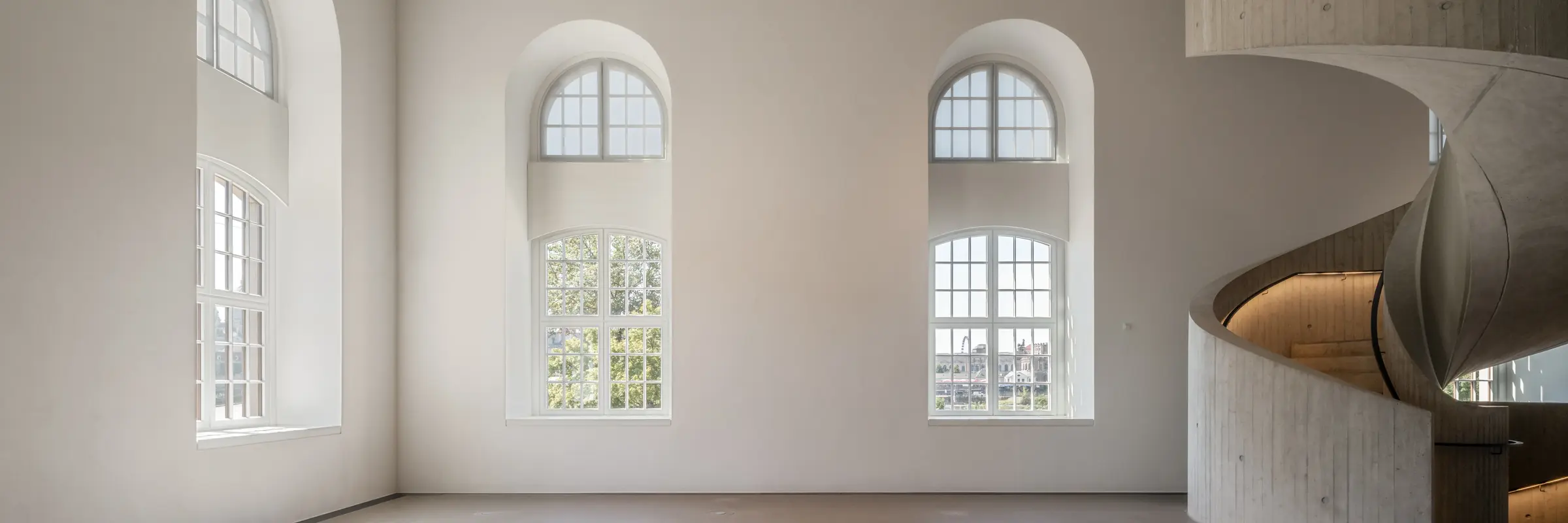 Ein lichtdurchfluteter Raum mit hohen Fenstern und einer geschwungenen Treppe.