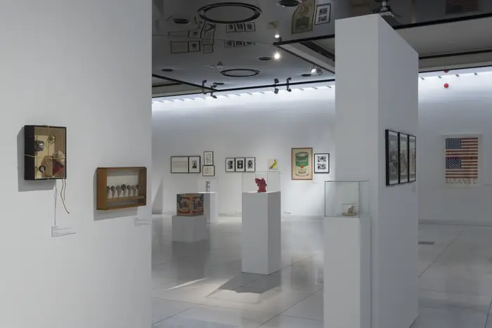 Eine Ausstellungsansicht mit an der Wand hängenden Bildern und Installationen