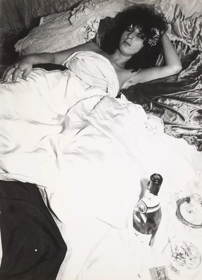 Frau liegt in einem Bett, vorne eine Champagnerflasche