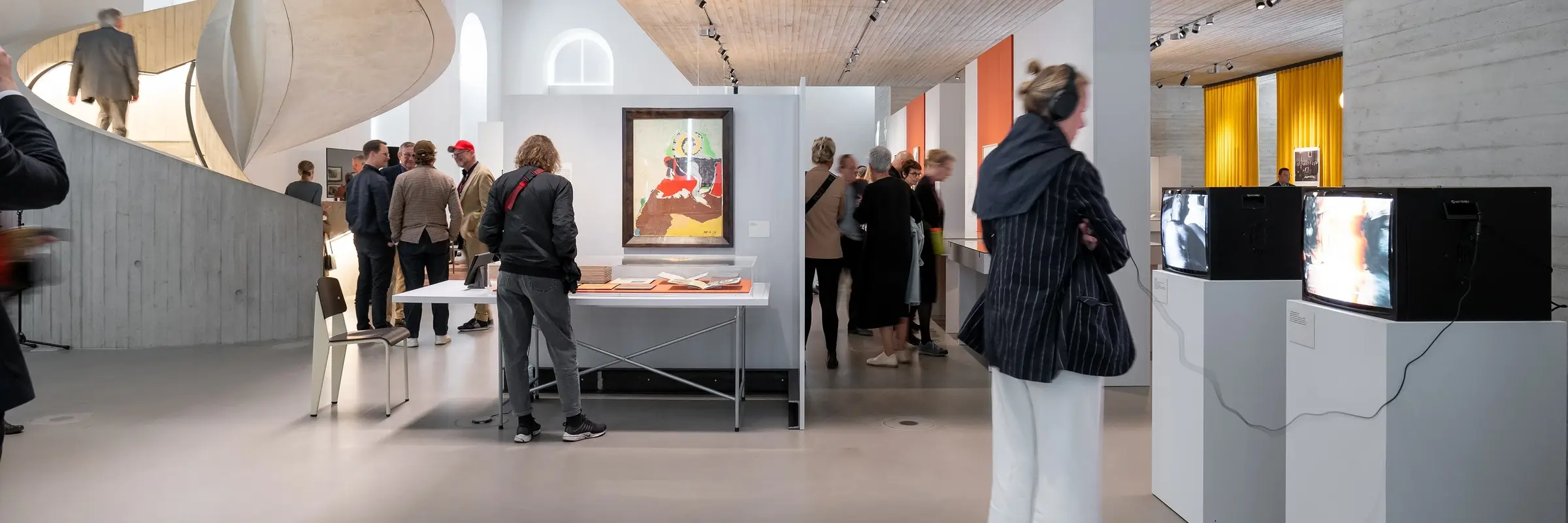 Menschen in einem Ausstellungsraum mit kleinen Fernsehgeräten.
