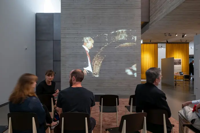 Besucher sitzen vor einer Projektion in einem Ausstellungsraum.