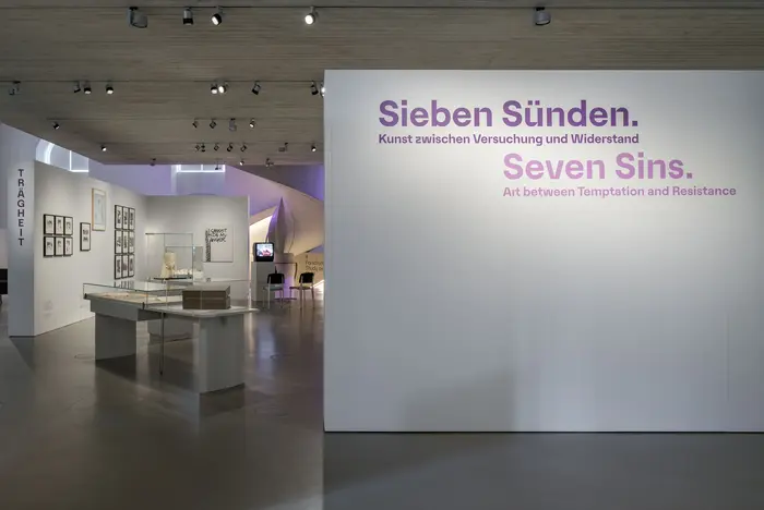 Blick in einen Raum, im Vordergrund eine Stellwand mit der Aufschrift "Sieben Sünden"
