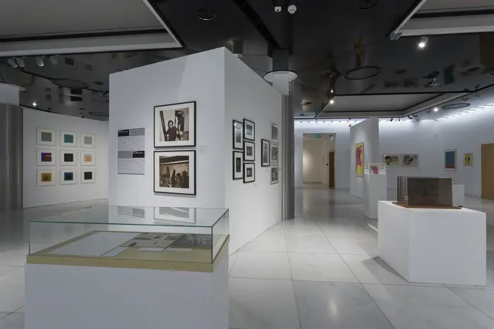 Eine Ausstellungsansicht mit an der Wand hängenden Bildern und einer Vitrine im Vordergrund