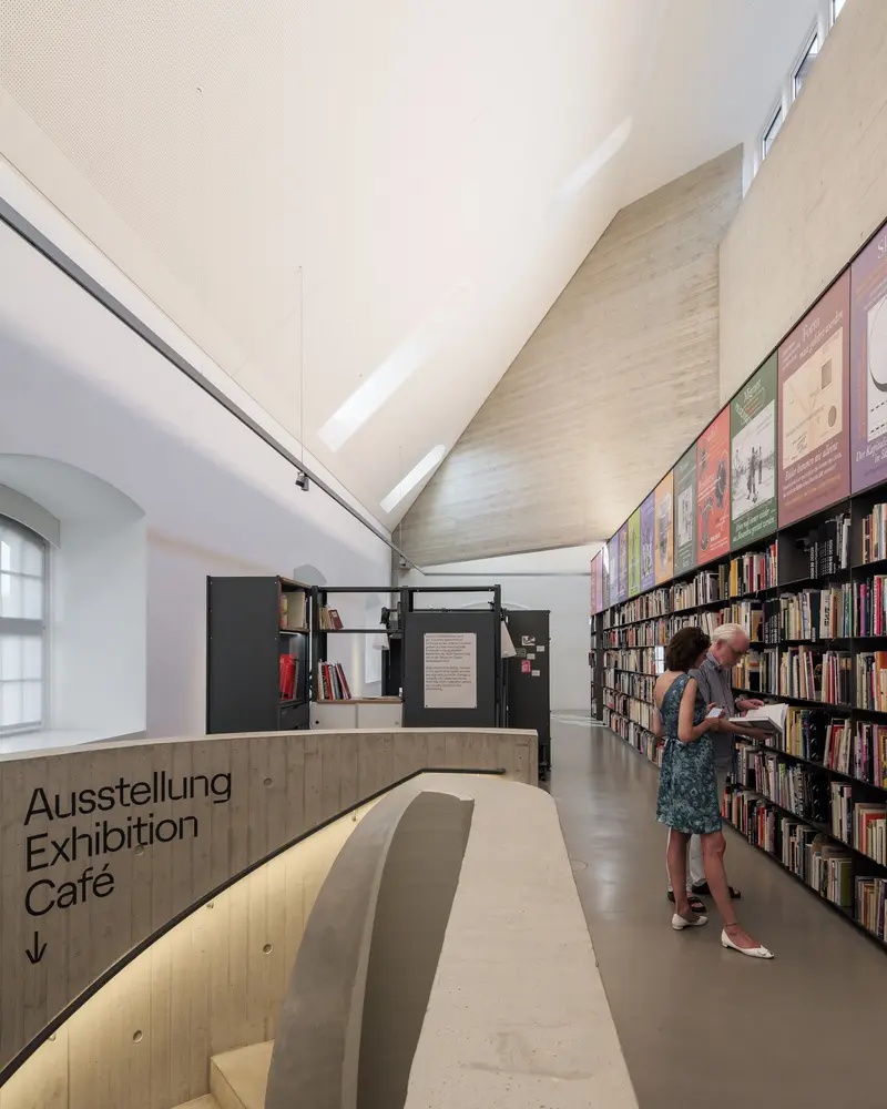 Ein Raum dessen eine Wand von einem Bücherregal bedeckt ist.