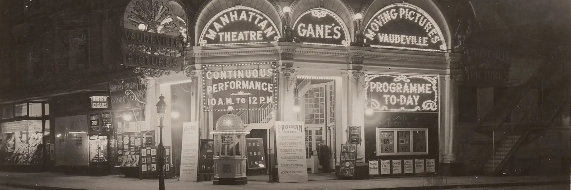 Ein schwarz-weißes Foto zeigt ein Theater in der Nacht. Seine Fassade ist belichtet durch Laterne. 