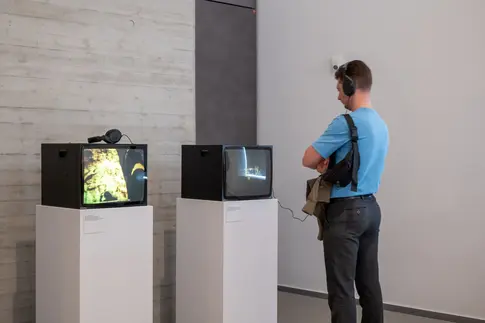 Ein Besucher schaut einen Film auf einem Fernsehgerät in einem Ausstellungsraum.